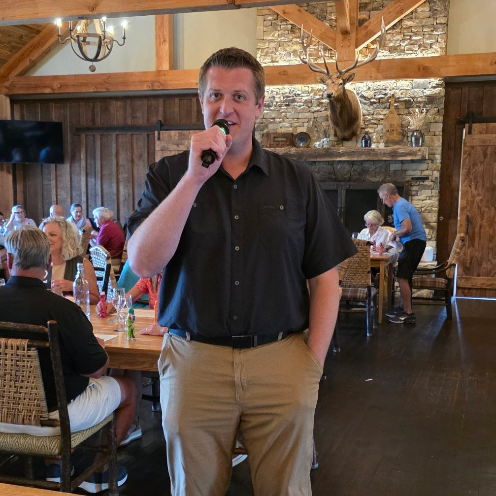 Man standing in a rustic wooden interior setting with a microphone.